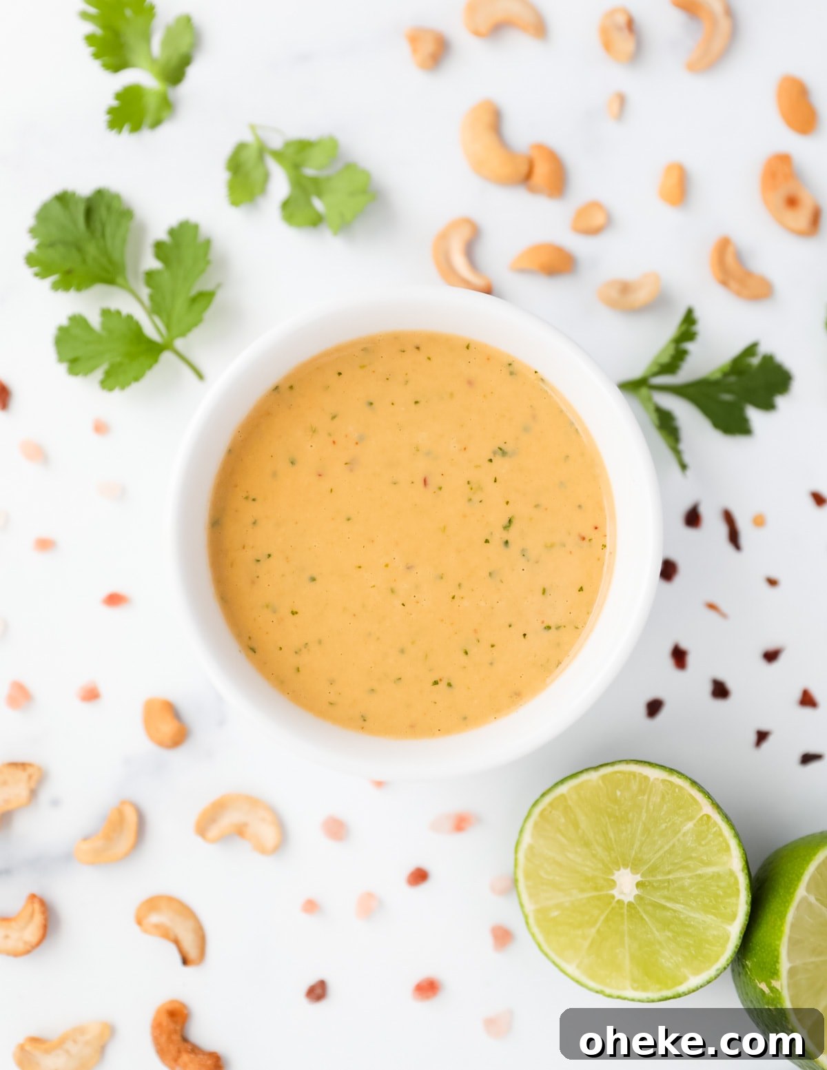 A white dish filled with a creamy, orange cashew salad dressing. There are ingredients around the bowl of dressing