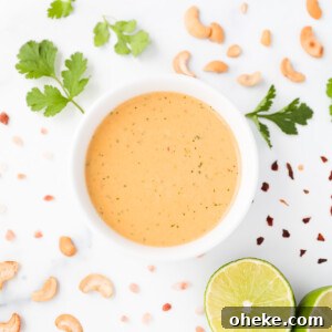 A creamy orange salad dressing in a white bowl with cilantro, cashews, red pepper flakes, a sliced lime, and salt