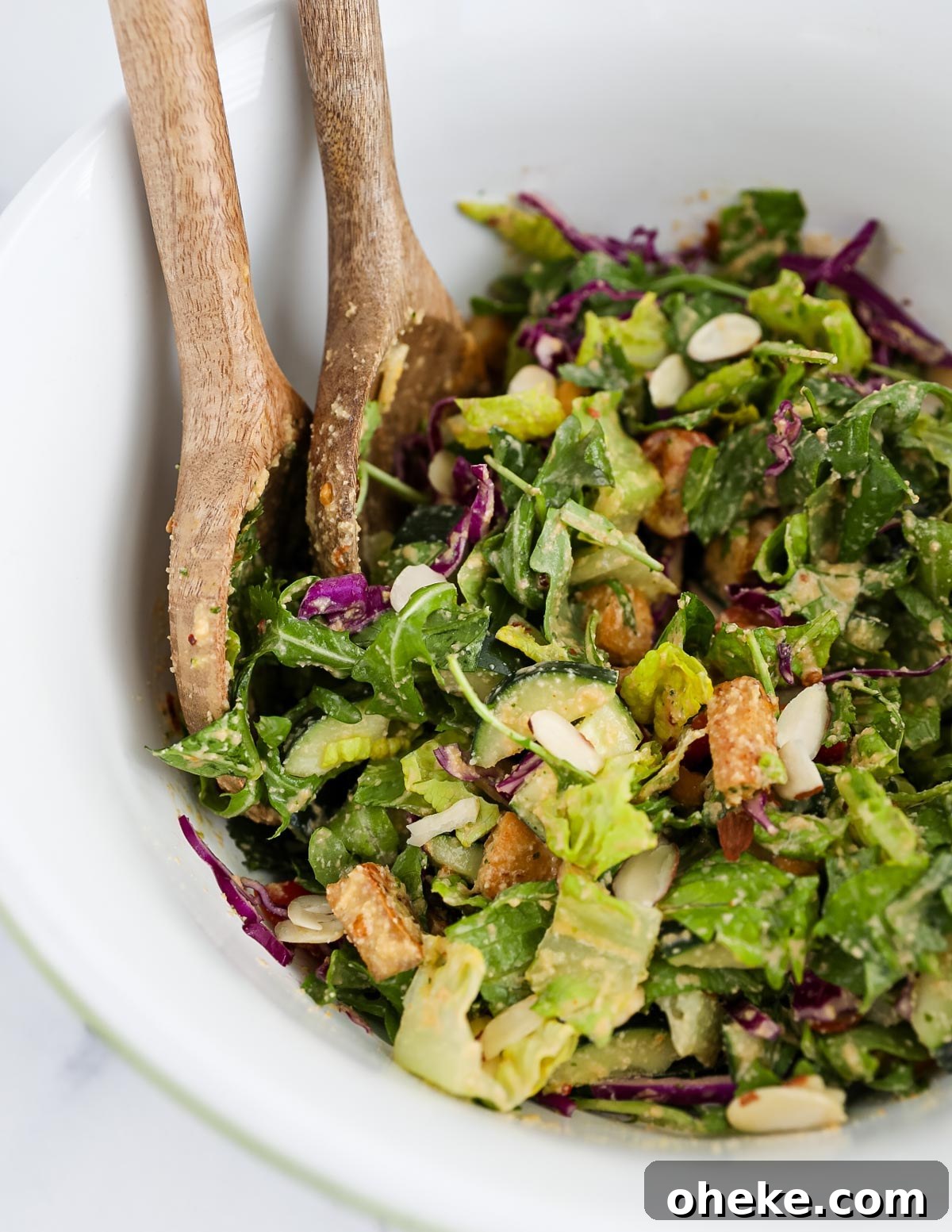 A large salad topped with creamy cashew dressing and two salad tongs