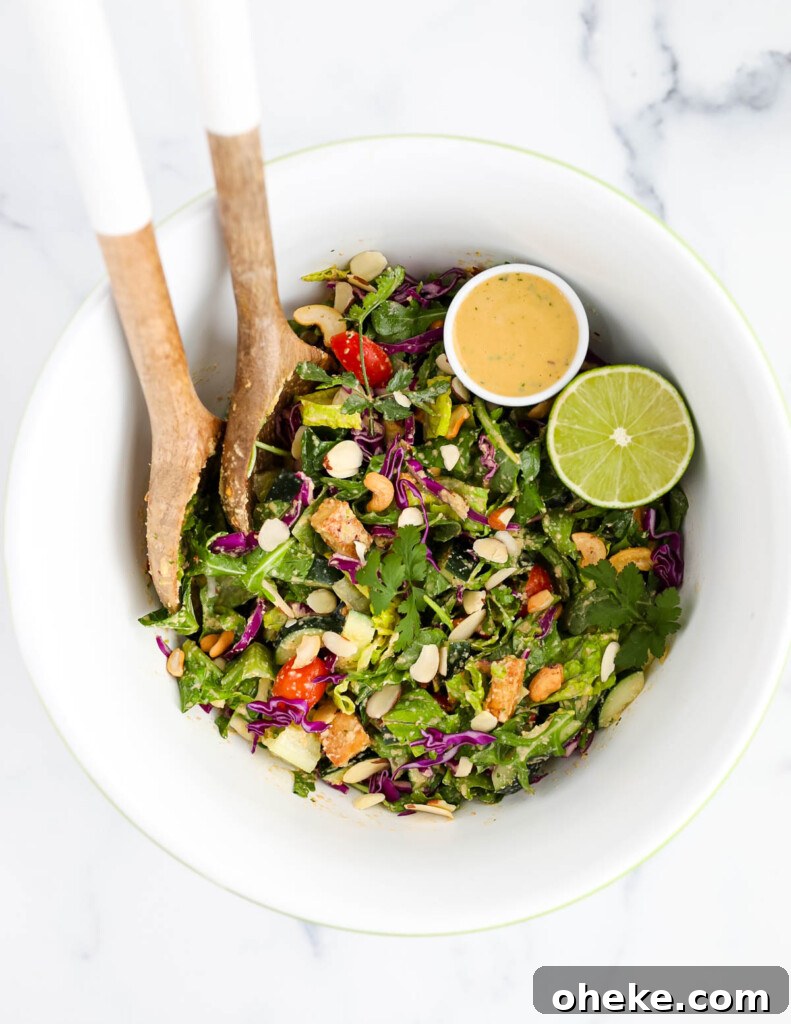 A large cashew salad in a white bowl with tofu, cabbage, almonds, cashews, lime, and dressing