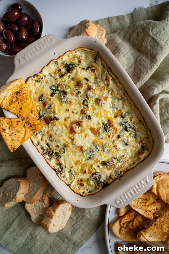 Creamy Baked Spanakopita Dip with Spinach & Feta 2 Baked spanakopita dip in a white casserole dish, with 2 baked pita chips on it.