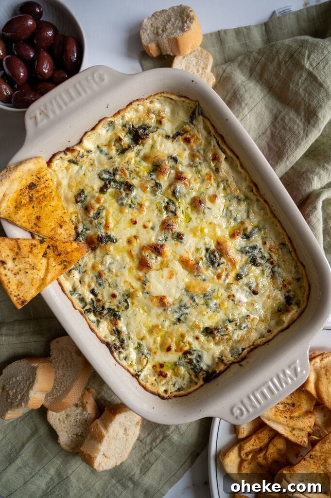 Creamy Baked Spanakopita Dip with Spinach & Feta 11 Baked spanakopita dip in a white casserole dish, with 2 baked pita chips on it.