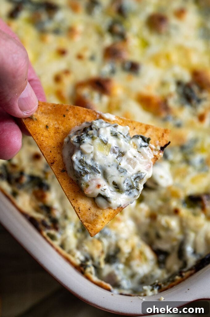 Creamy Baked Spanakopita Dip with Spinach & Feta 12 Dipping a pita chip into the baked spanakopita dip.