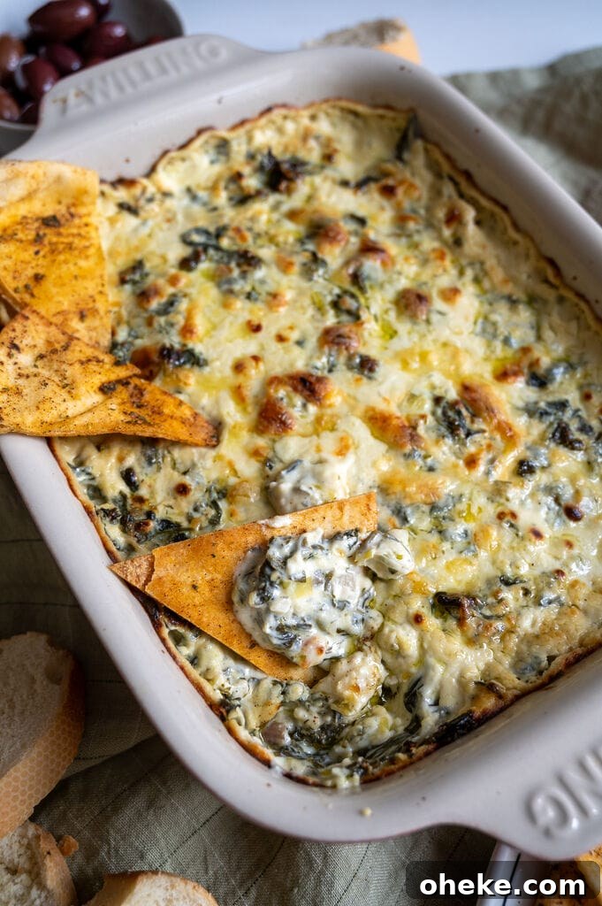 Creamy Baked Spanakopita Dip with Spinach & Feta 13 Baked spanakopita dip in a white casserole dish, with 3 baked pita chips on it.