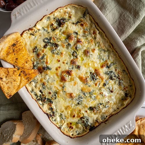 Creamy Baked Spanakopita Dip with Spinach & Feta 14 Baked spanakopita dip in a white casserole dish, with 2 baked pita chips on it.