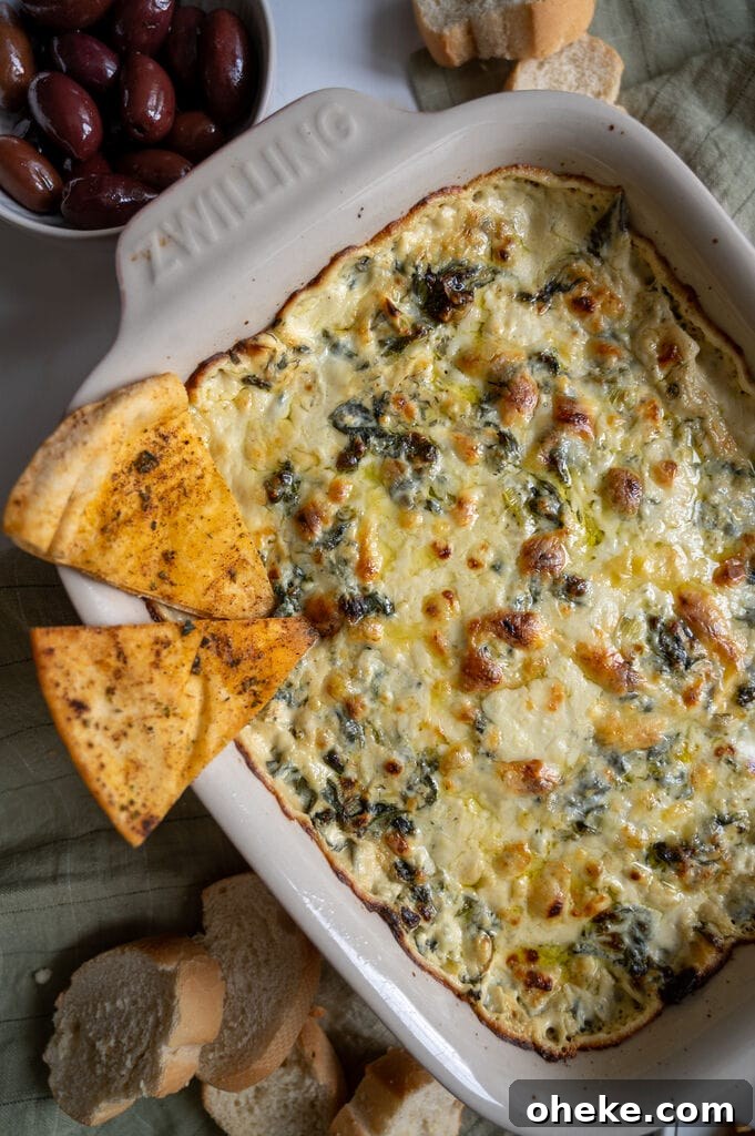 Creamy Baked Spanakopita Dip with Spinach & Feta 3 Baked spanakopita dip in a white casserole dish, with 2 baked pita chips on it.