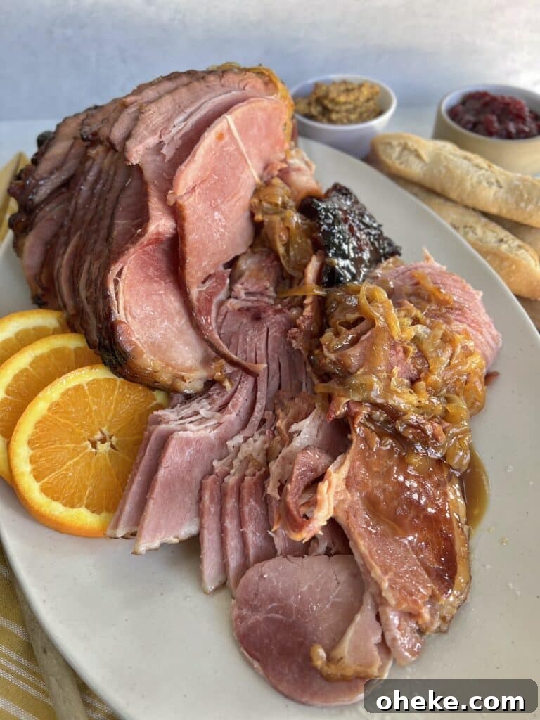 Dutch Oven Spiral Ham with Marsala Glaze Recipe 2 Baked ham in a dutch oven plated on an oval platter with orange slices and onions, with mustard, cranberry sauce and bread in the background.