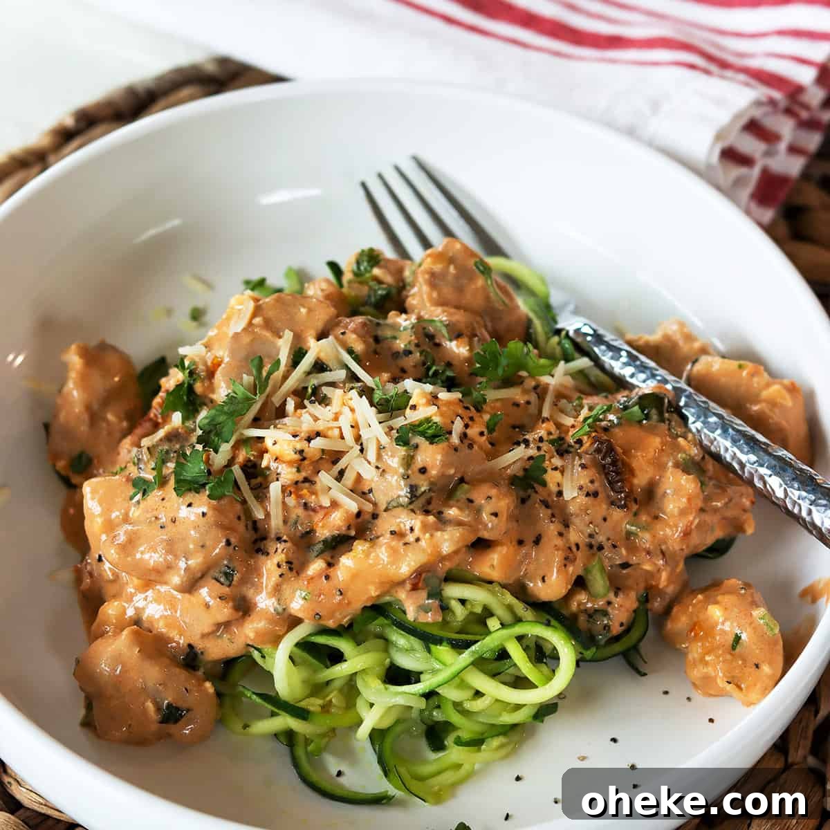 square feature image of low carb chicken in tomato basil cream sauce served on a white plate over zucchini noodles and garnished with extra cheese and parsley.