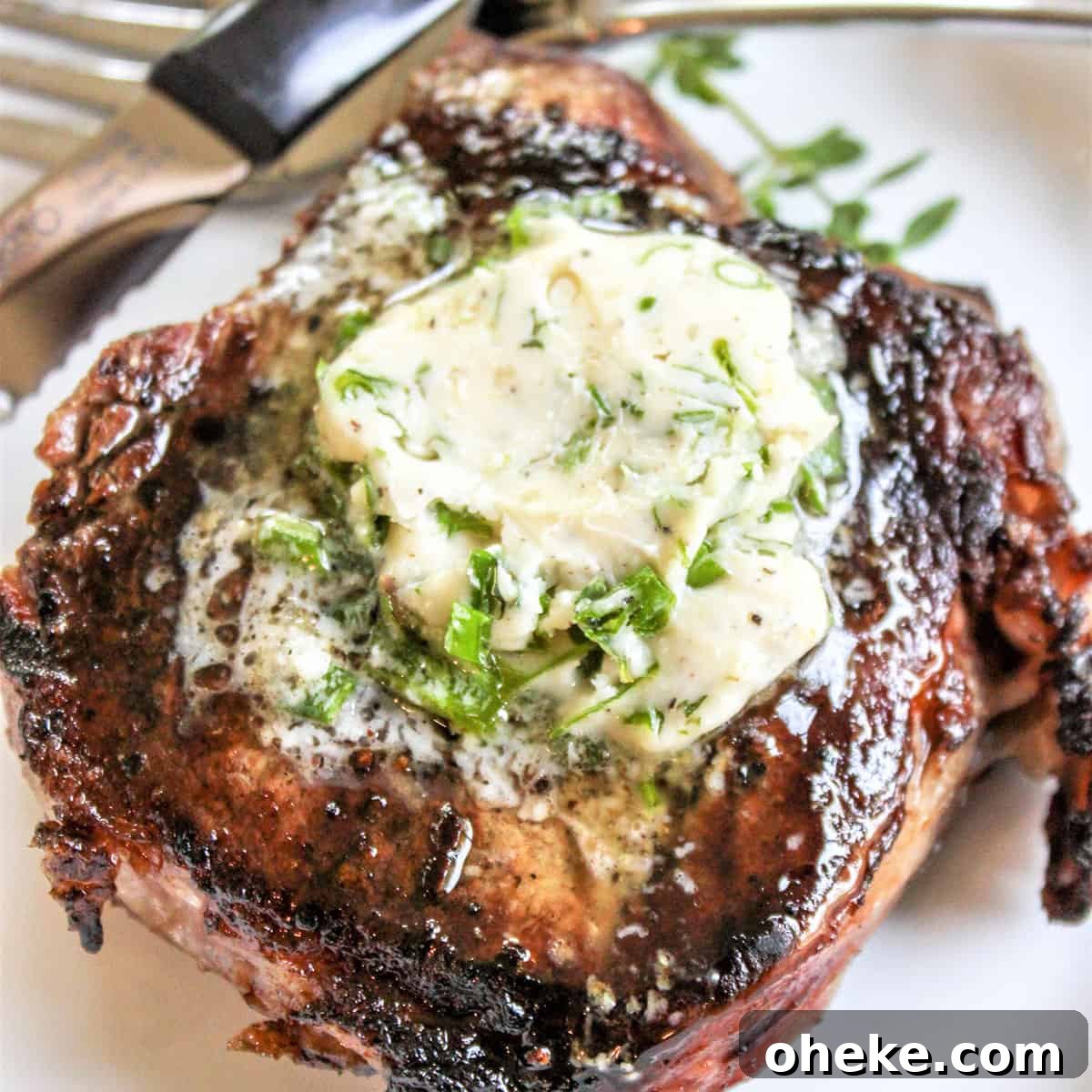 Closeup image of grilled steak with a pat of melting herbed compound butter on top.