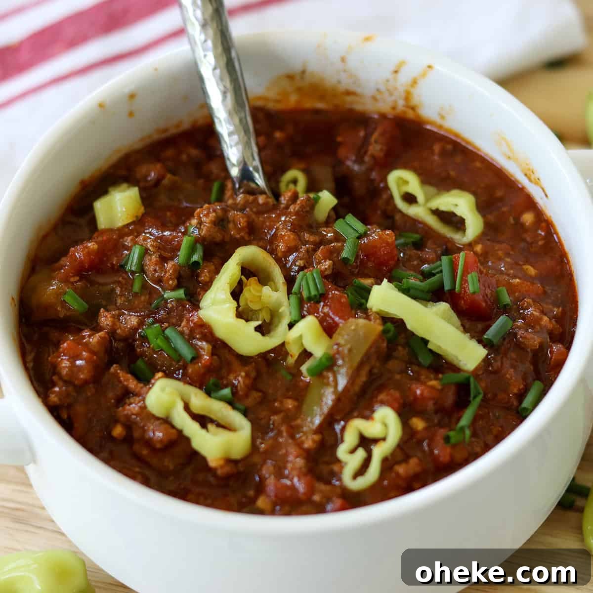 Square image closeup of finished chili served in a white bowl and garnished with pepperoncini.