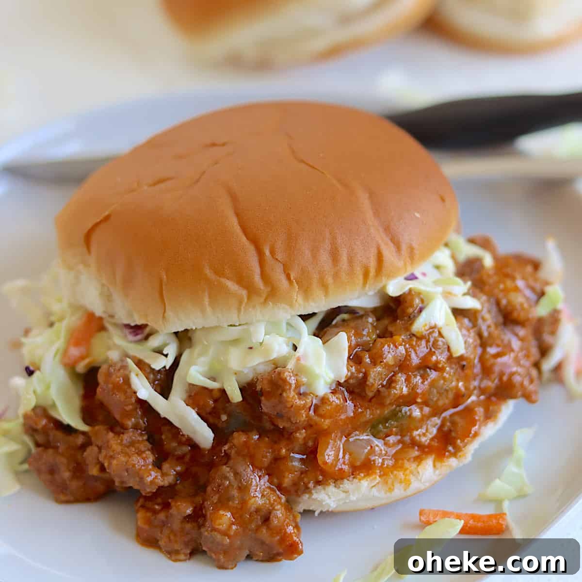 A white plate with slow cooker sloppy joes served on a hamburger bun with coleslaw.