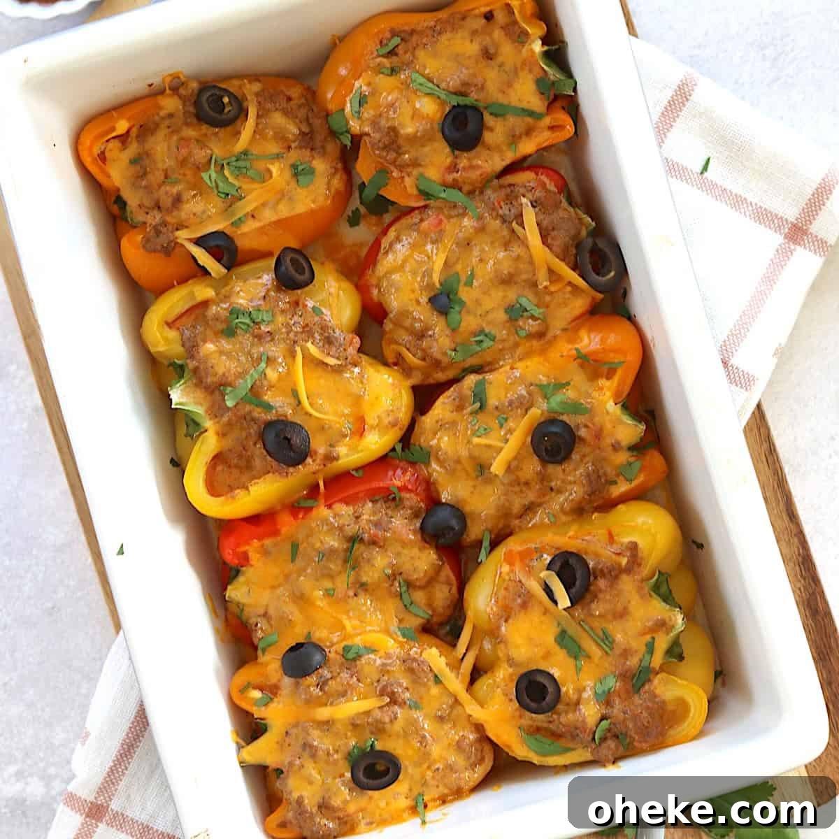 A white baking dish of stuffed taco peppers with melted cheese and olives on top.