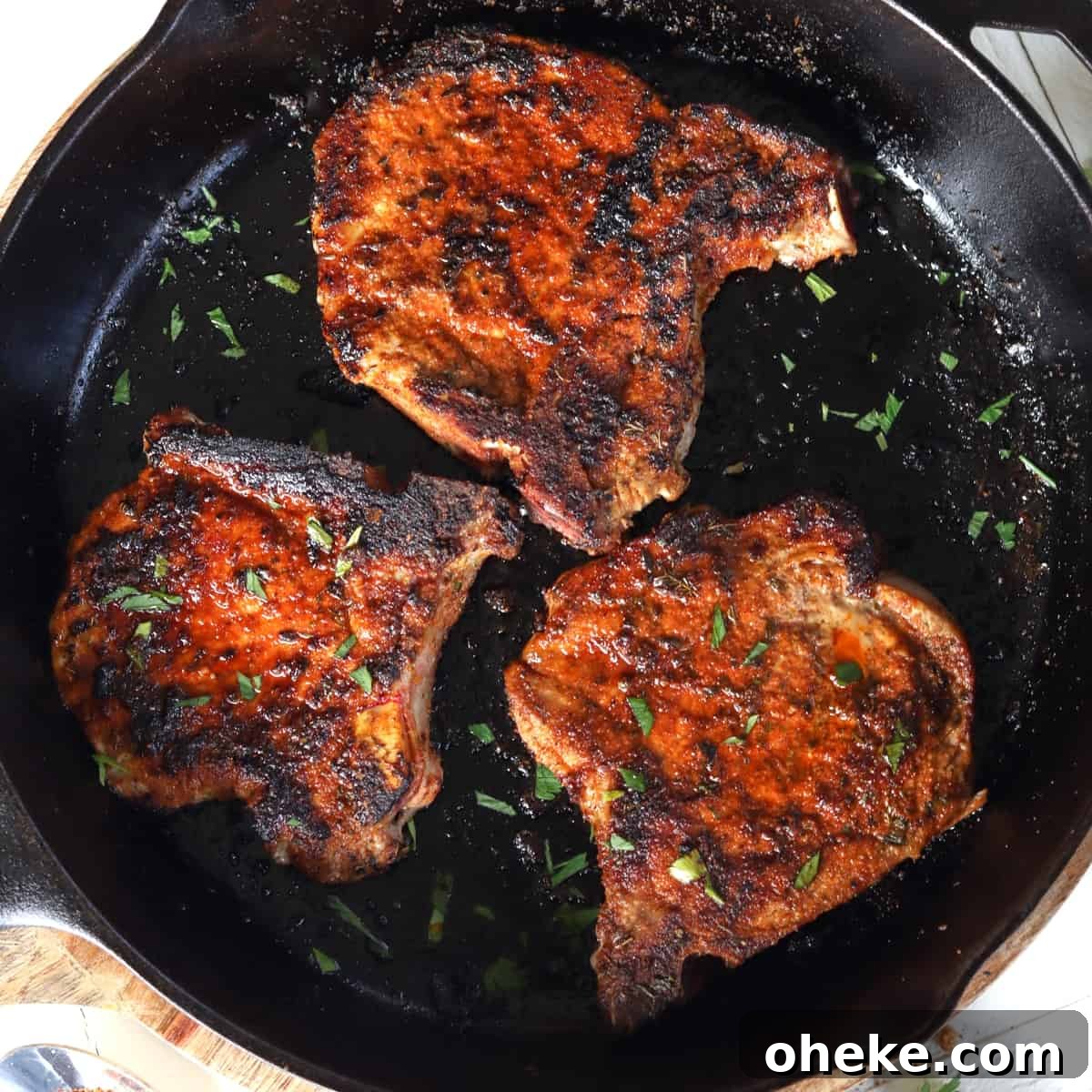 Square image of a cast iron skillet with three pan seared dry rubbed pork chops