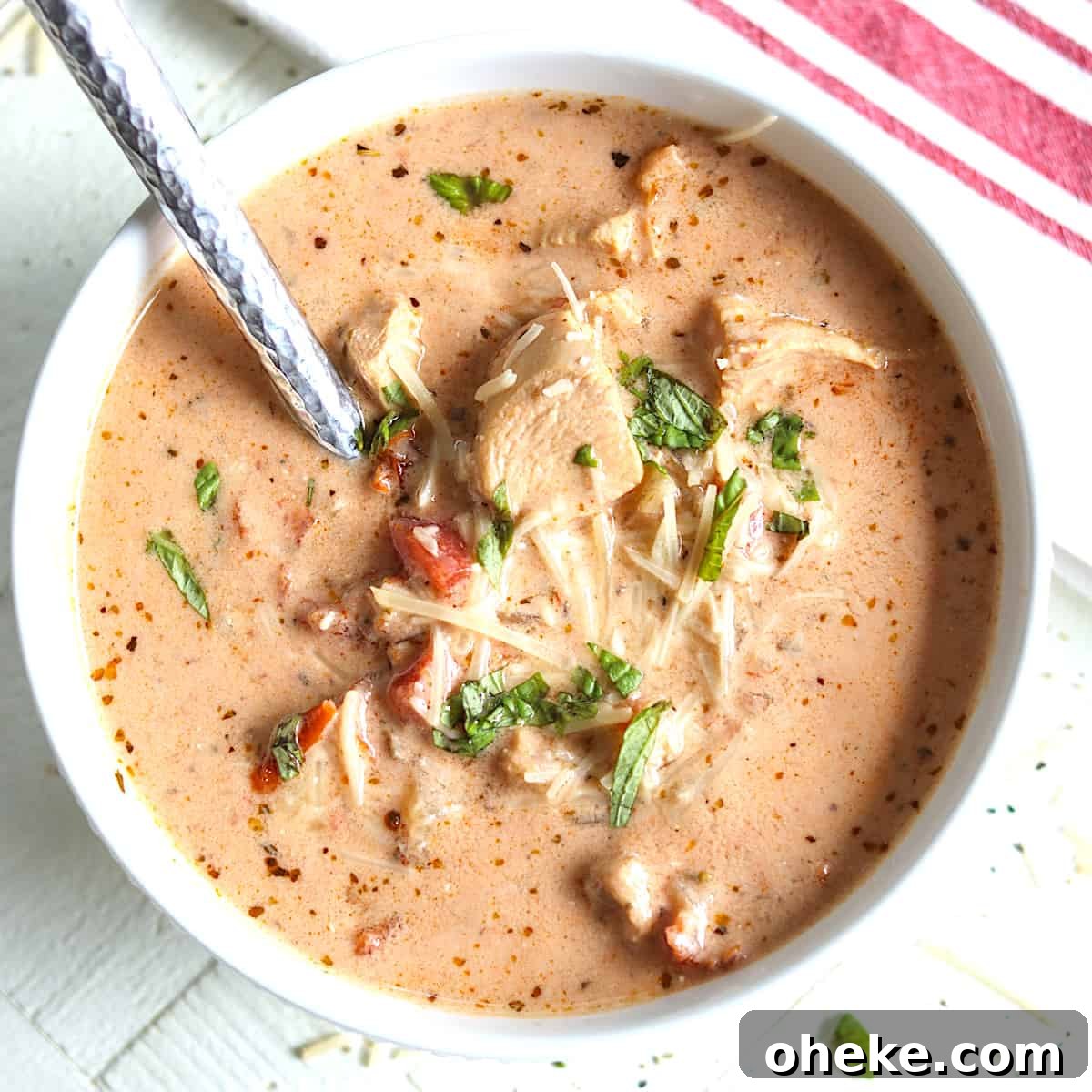 A white bowl full of tomato chicken soup garnished with fresh basil.