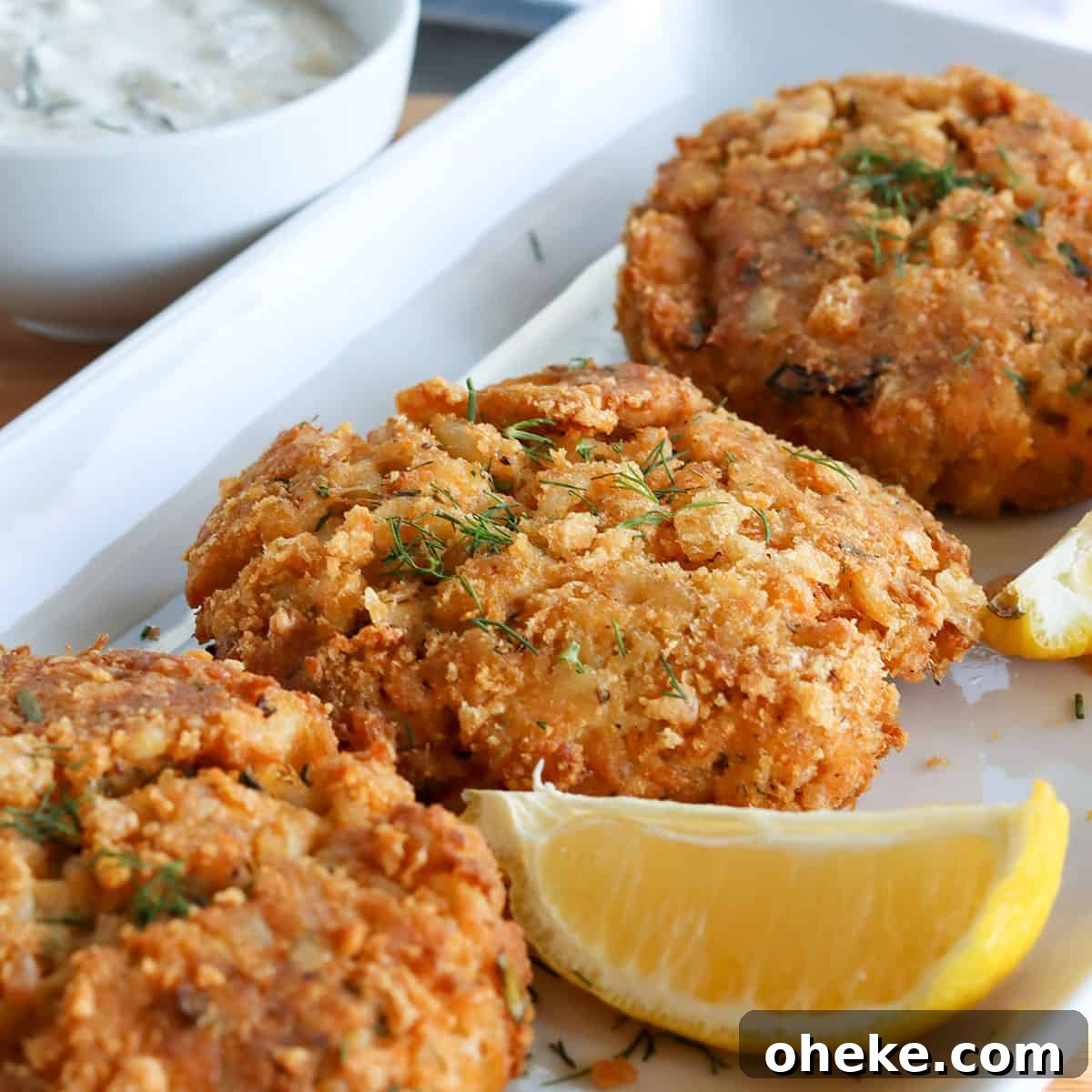 Air fryer crab cakes served on a white platter with lemon wedges and creamy dill dressing for dipping.