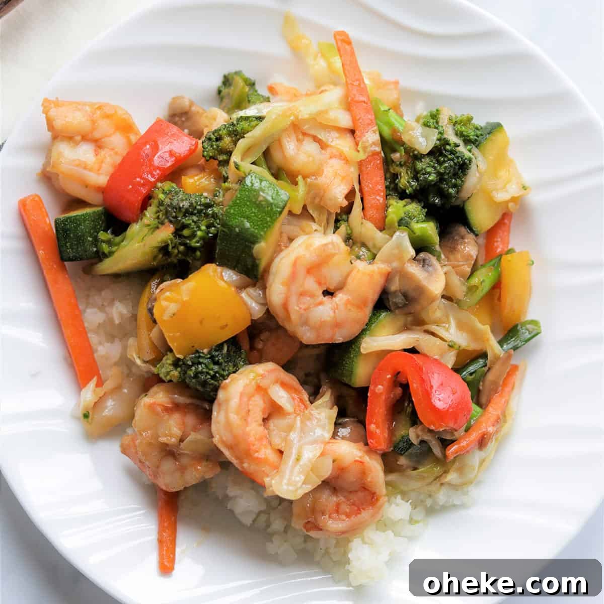 closeup image of shrimp stir fry served on a white plate over cauliflower rice