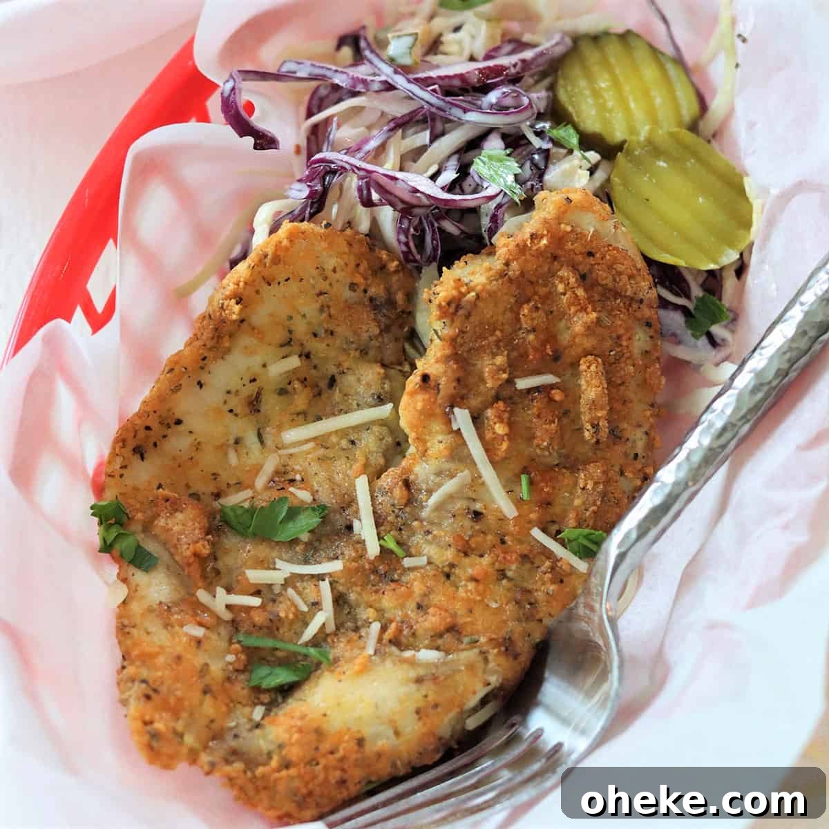 Looking down on a piece of air tilapia with a parmesan crust, a side of coleslaw in a red basket with white parchment paper