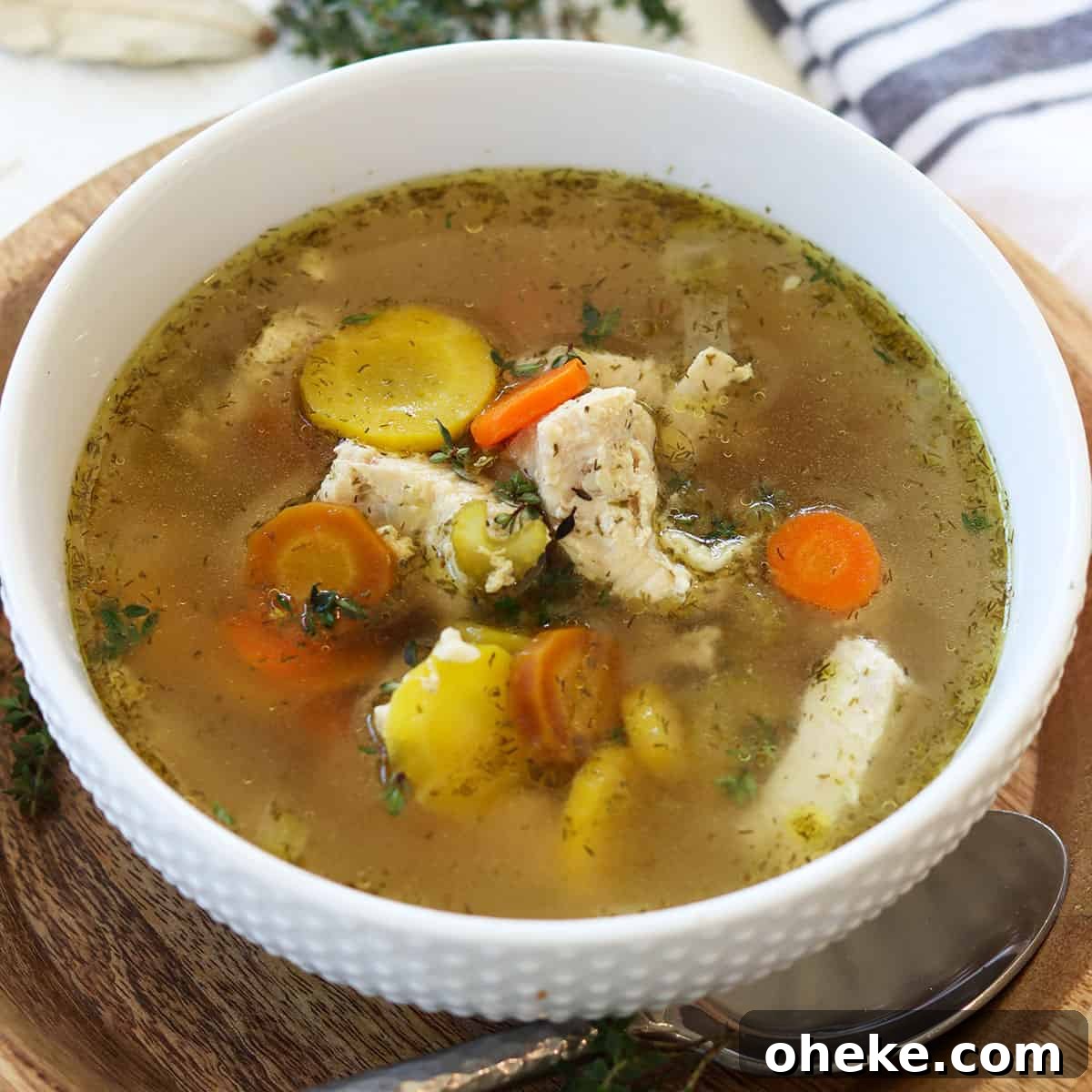 A white bowl full of instant pot chicken soup garnished with fresh herbs.