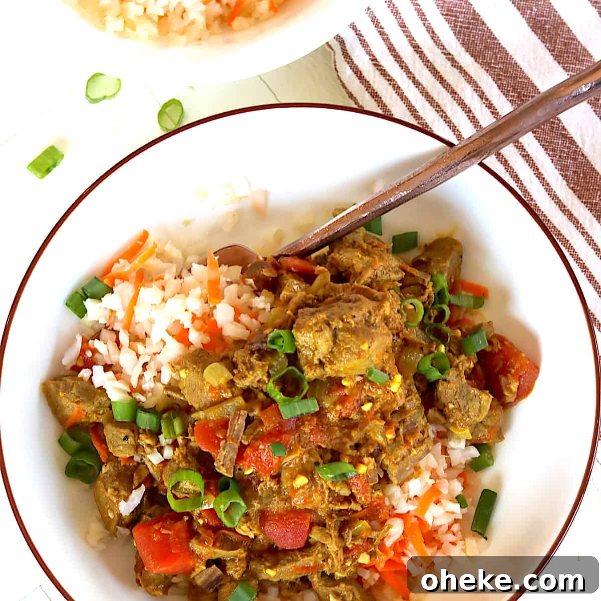 A white bowl with lamb curry served over riced cauliflower with shredded carrots.