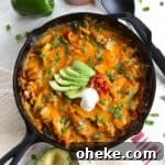 Baked chicken fajita casserole in a cast iron skillet with slices of avocado, sour cream, salsa, and fresh cilantro.
