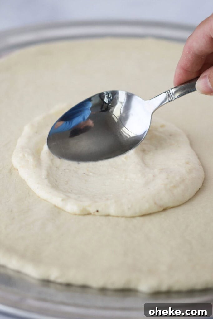 A spoon spreading this white sauce recipe for pizza over pizza dough.