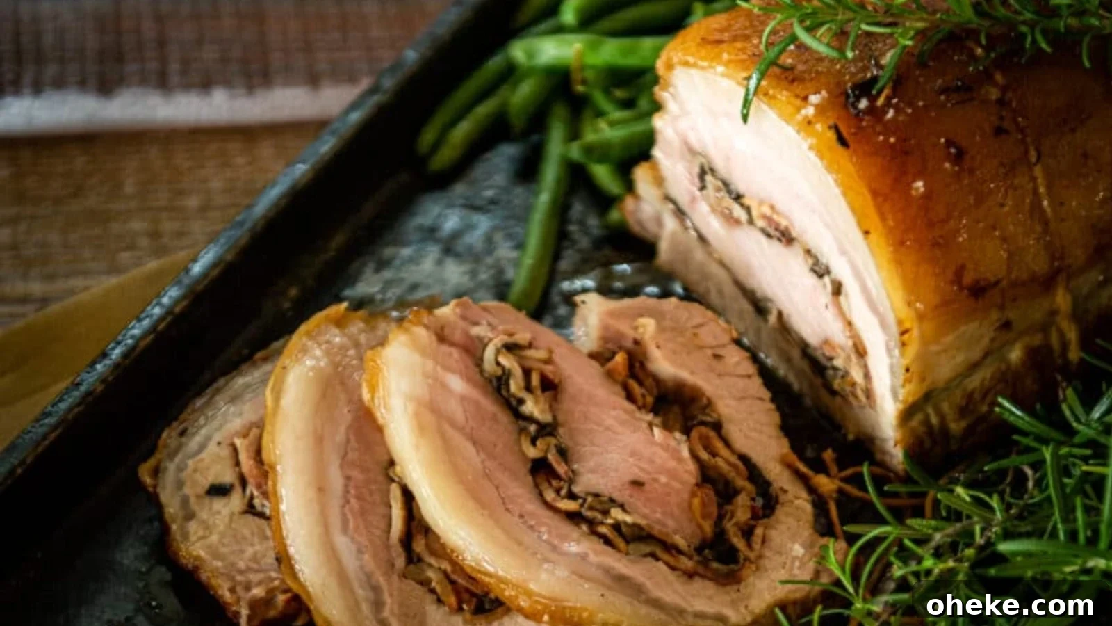 A close-up of sliced rolled pork roast with a herb and mushroom filling, served with green beans and garnished with fresh rosemary.
