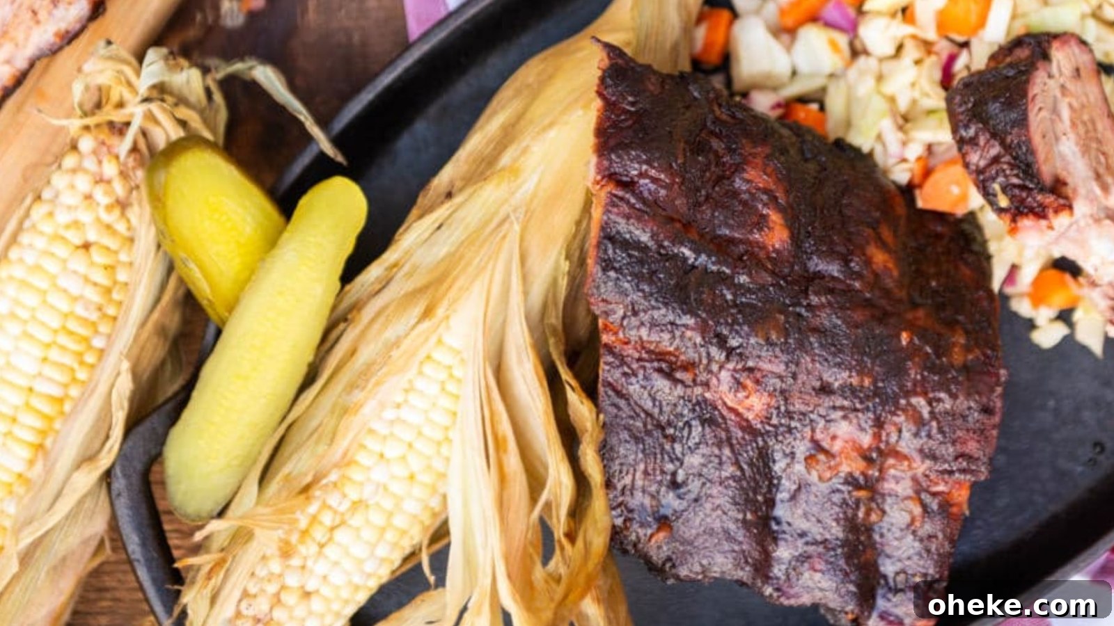 A plate with grilled corn on the cob, pickles, coleslaw, and a portion of barbecued ribs.