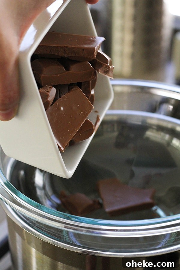 Crunchy Chocolate-Covered Almonds Recipe for Homemade Snacks 6 A hand pouring a bowl of chopped chocolate into a glass bowl over a saucepan.