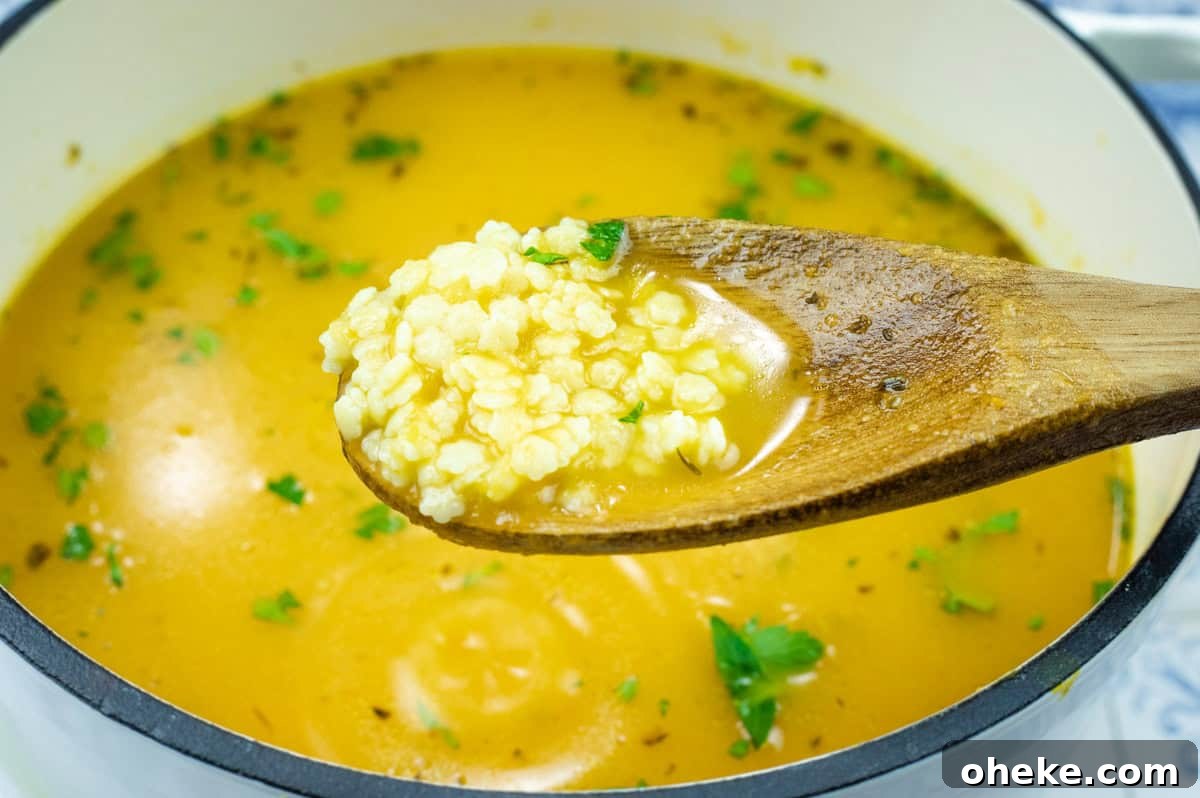 A wooden spoon holds a portion of Pastina Soup hovering above a pot.