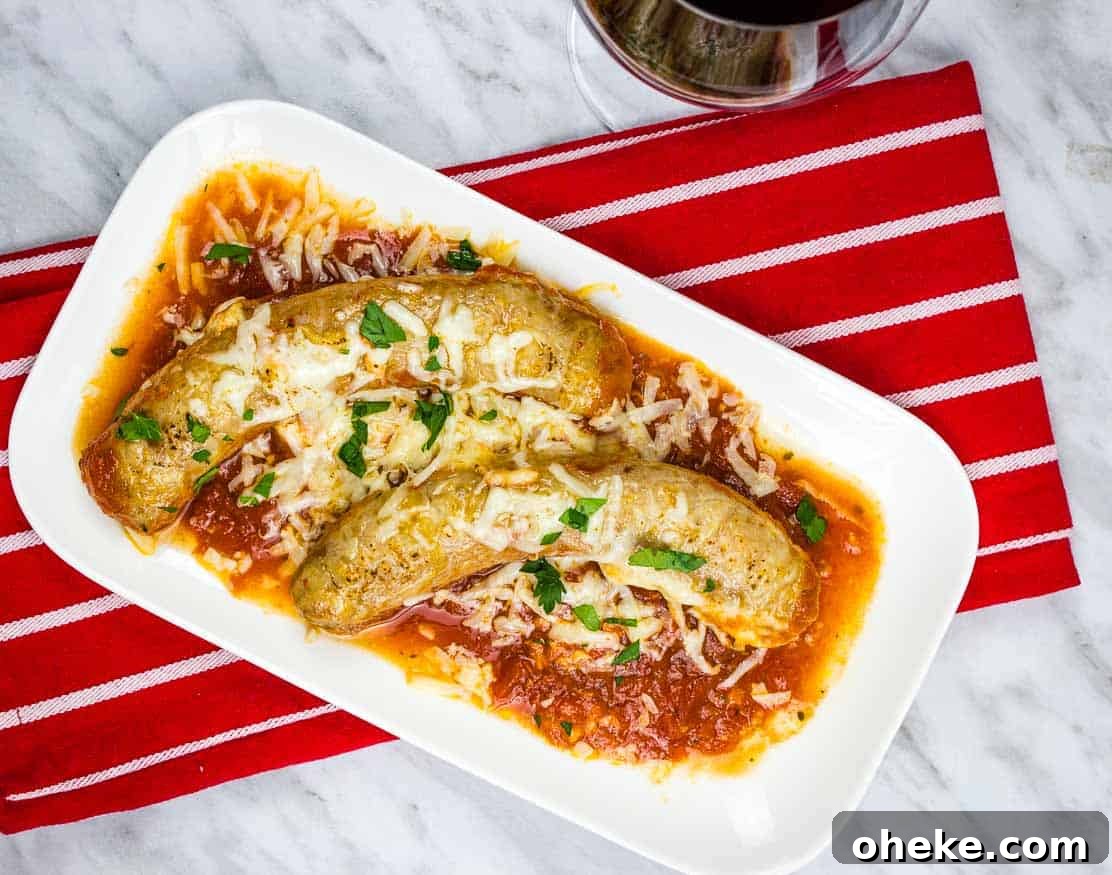 Two sausages topped with cheese and herbs on tomato sauce, served on a white plate over a red striped napkin, next to a glass of red wine.