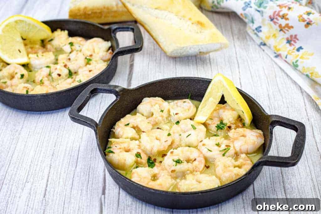 Two cast iron skillets contain shrimp scampi garnished with lemon wedges.