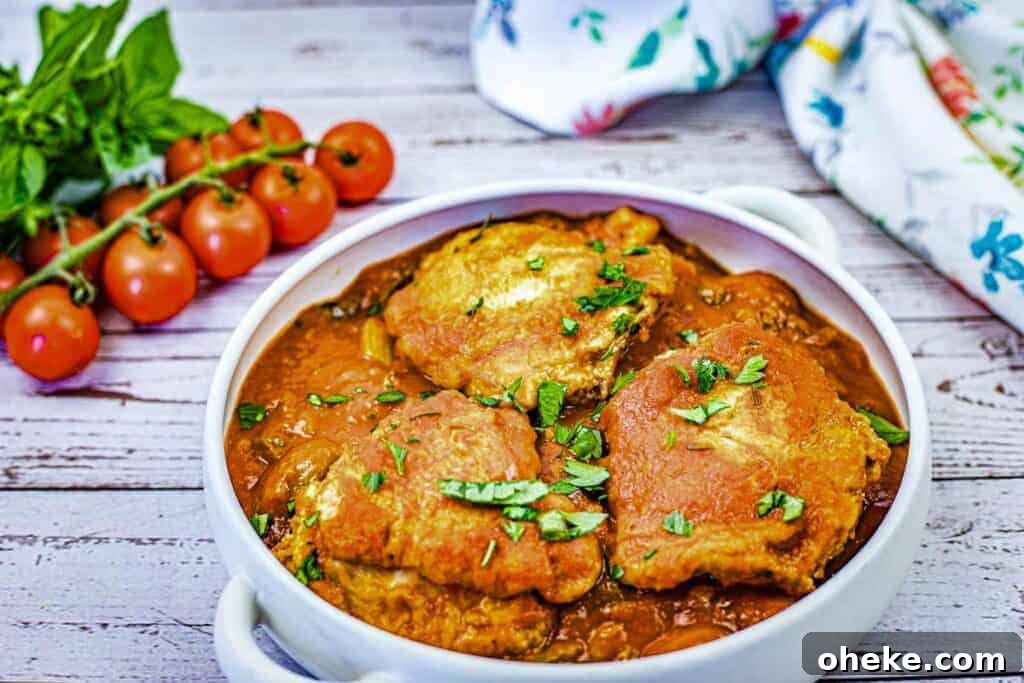 A white dish filled with pieces of Chicken Cacciatore in a red sauce, garnished with chopped herbs.