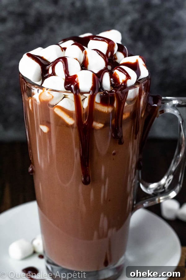 glass mug of hot chocolate topped with mini marshmallows and chocolate sauce