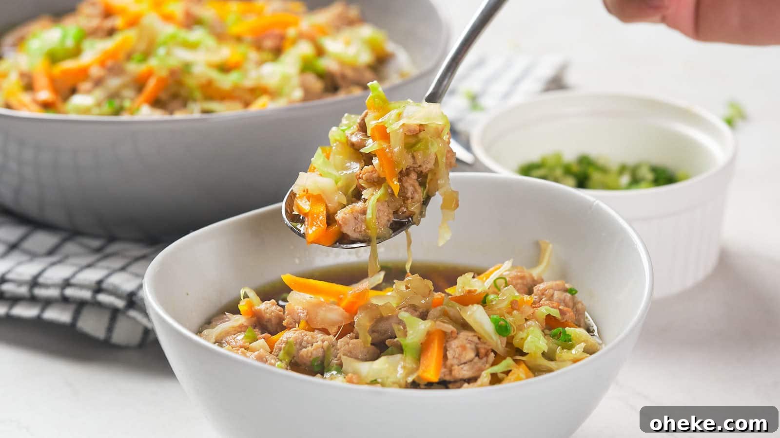 17 Comforting Recipes to Keep You Warm This Season 8 A hand holds a spoonful of egg roll soup over a white bowl.