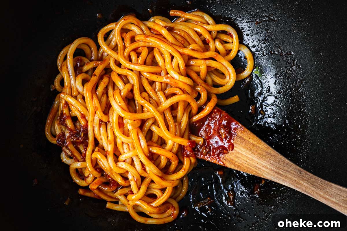 Spicy Gochujang Korean Noodles Recipe 10 Cooked udon noodles getting coated in gochujang noodle sauce in a wok.