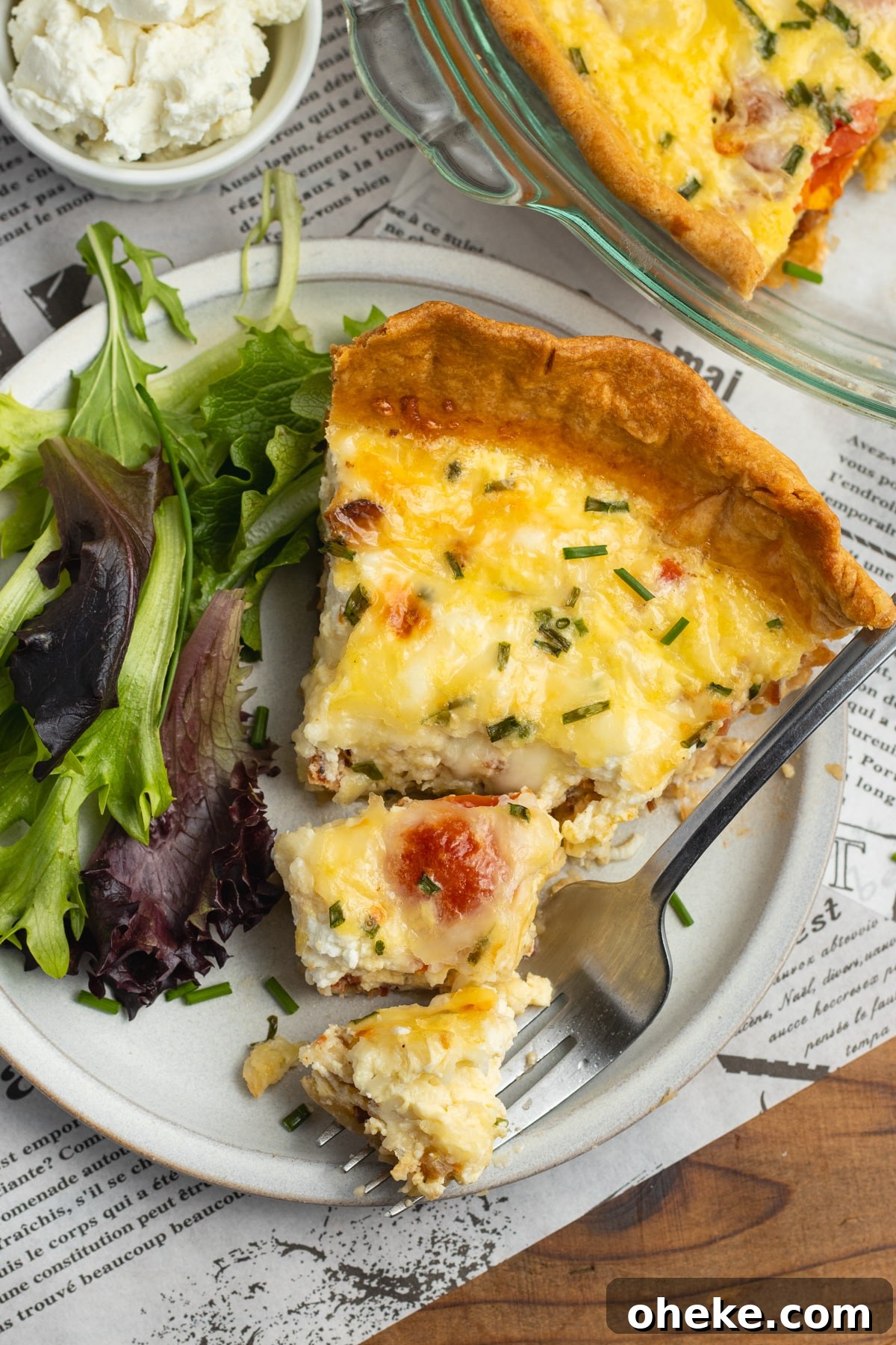 This is a picture of a plate with. a slice of tomato bacon goat cheese quiche with gruyere.