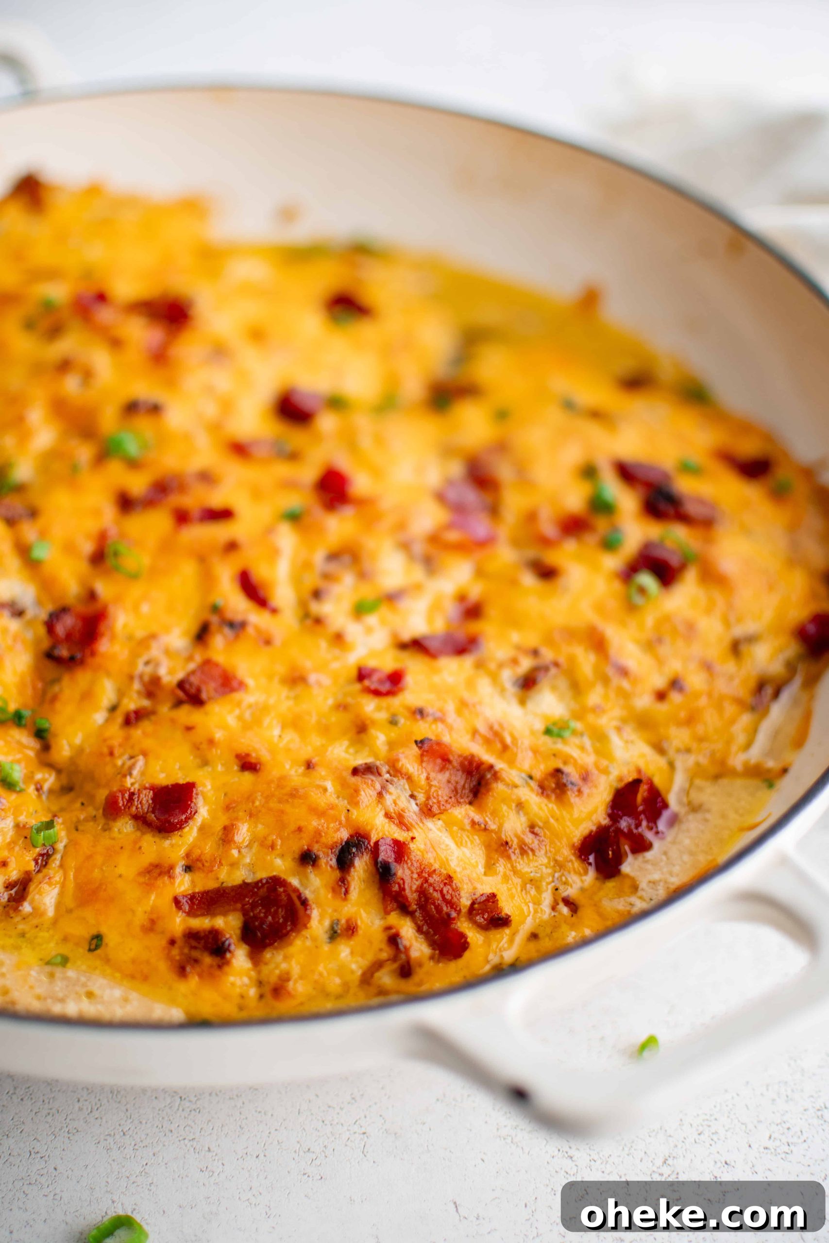 Large white oven-safe pan filled with chicken breasts covered in a mixture of cream of chicken soup, ranch seasoning mix, cream cheese, gooey melted cheddar cheese, and bacon bits.