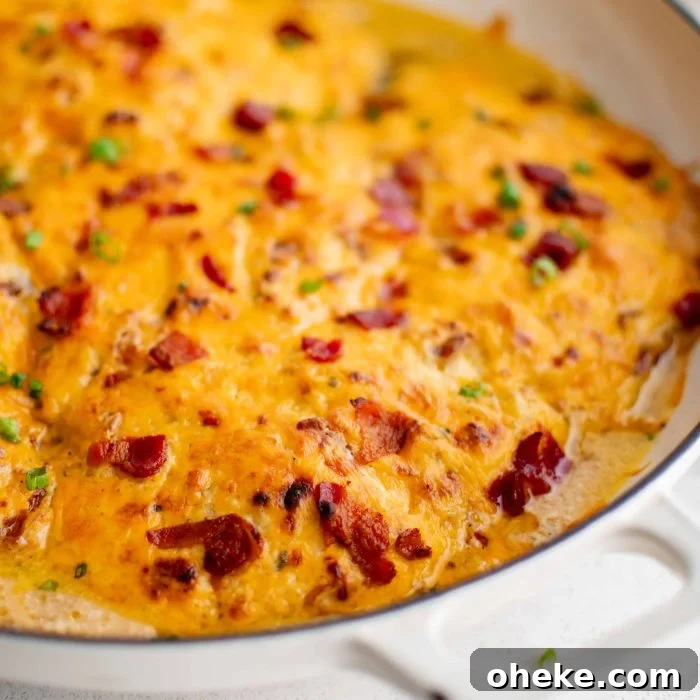 Large white oven-safe pan filled with chicken breasts covered in a mixture of cream of chicken soup, ranch seasoning mix, cream cheese, gooey melted cheddar cheese, and bacon bits.