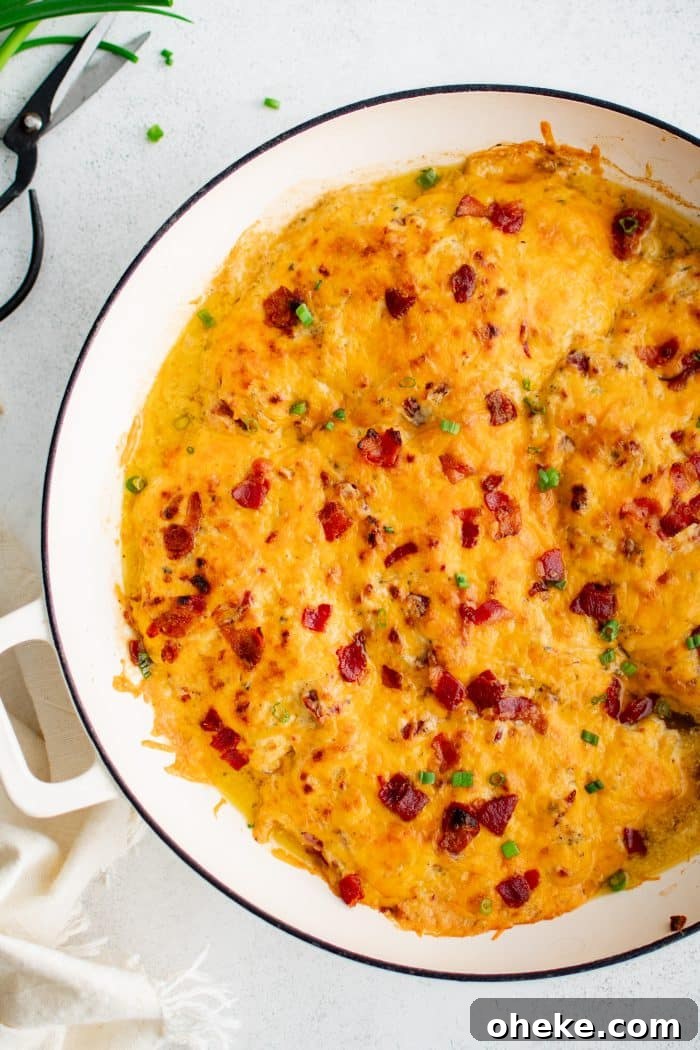 Large white oven-safe pan filled with chicken breasts covered in a mixture of cream of chicken soup, ranch seasoning mix, cream cheese, gooey melted cheddar cheese, and bacon bits.