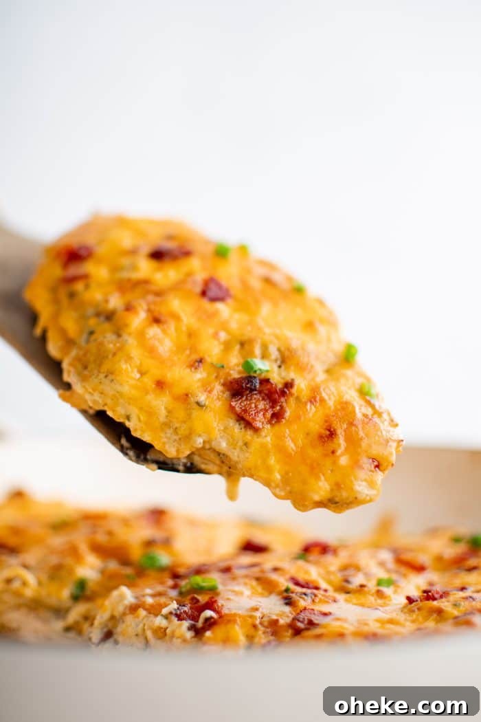 Wooden serving spatula removing a baked chicken breast covered with 'crack' chicken mixture.