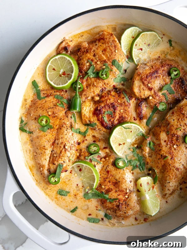 Large white enameled skillet filled with thinly sliced chicken breasts simmering in a homemade sauce made with coconut milk and lime.