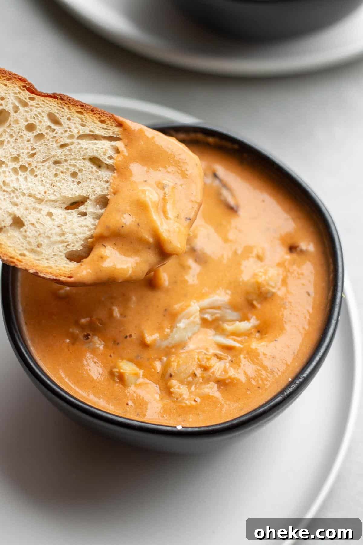 A black bowl with a crab bisque and a piece of sourdough scooping some out.