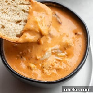 A black bowl with a crab bisque and piece of sourdough being dunked in it.