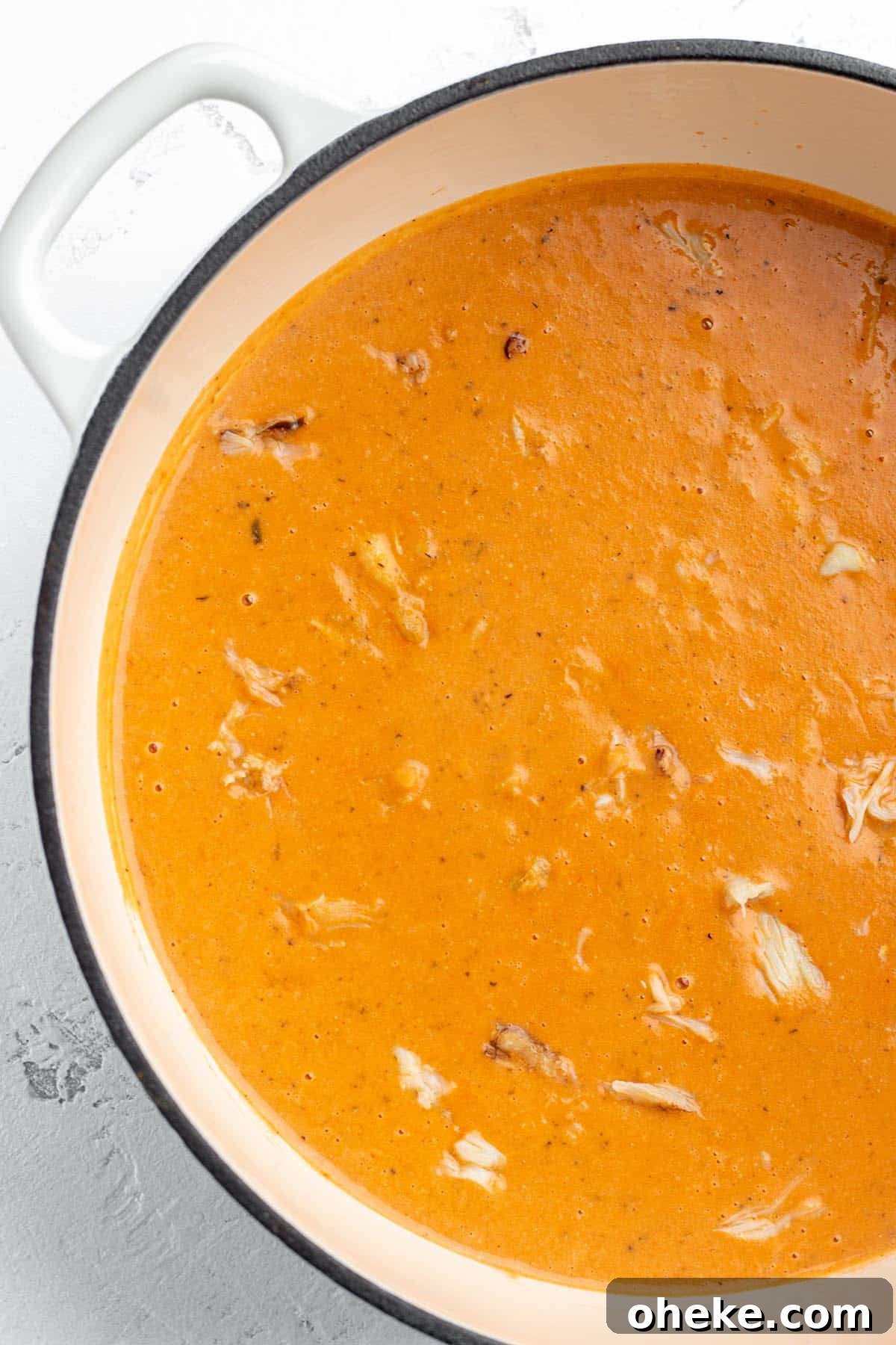 A white Dutch Oven with a tomato bisque with lumps of crab meat.