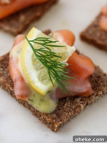 Close up of gravlax on rye bread topped with a lemon wedge and fresh dill.