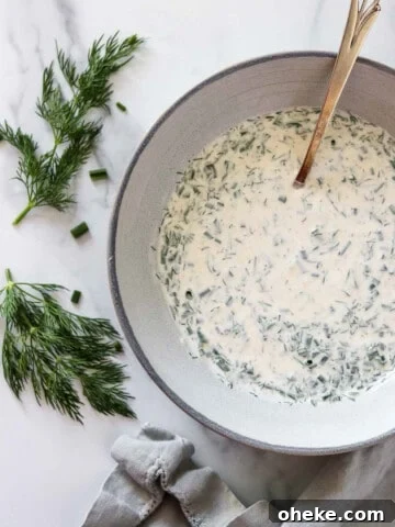A bowl with herbed yogurt sauce next to fresh dill sprigs and a napkin.