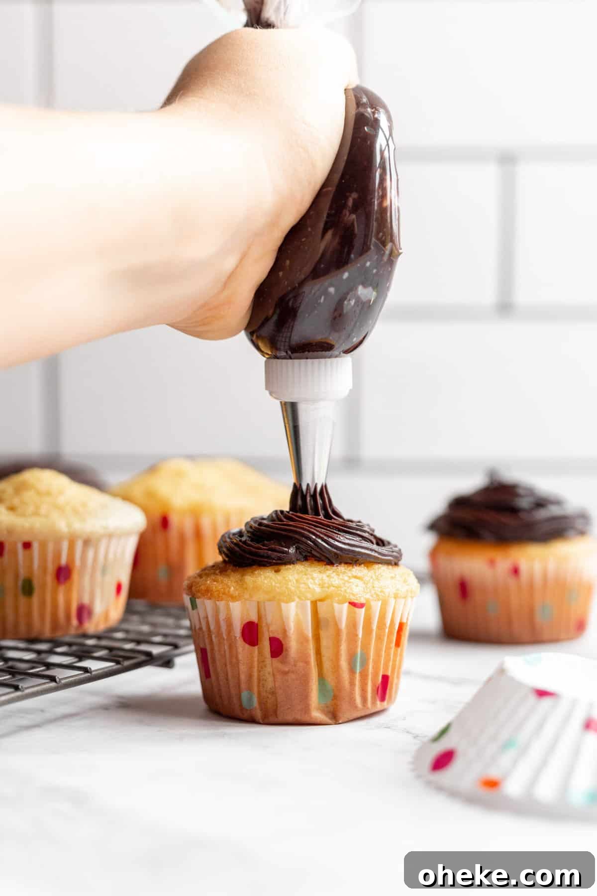 Top Cake Decorating Tools: 12 Must-Have Supplies for Bakers 2 chocolate frosting in a piping bag decorating a vanilla cupcake.