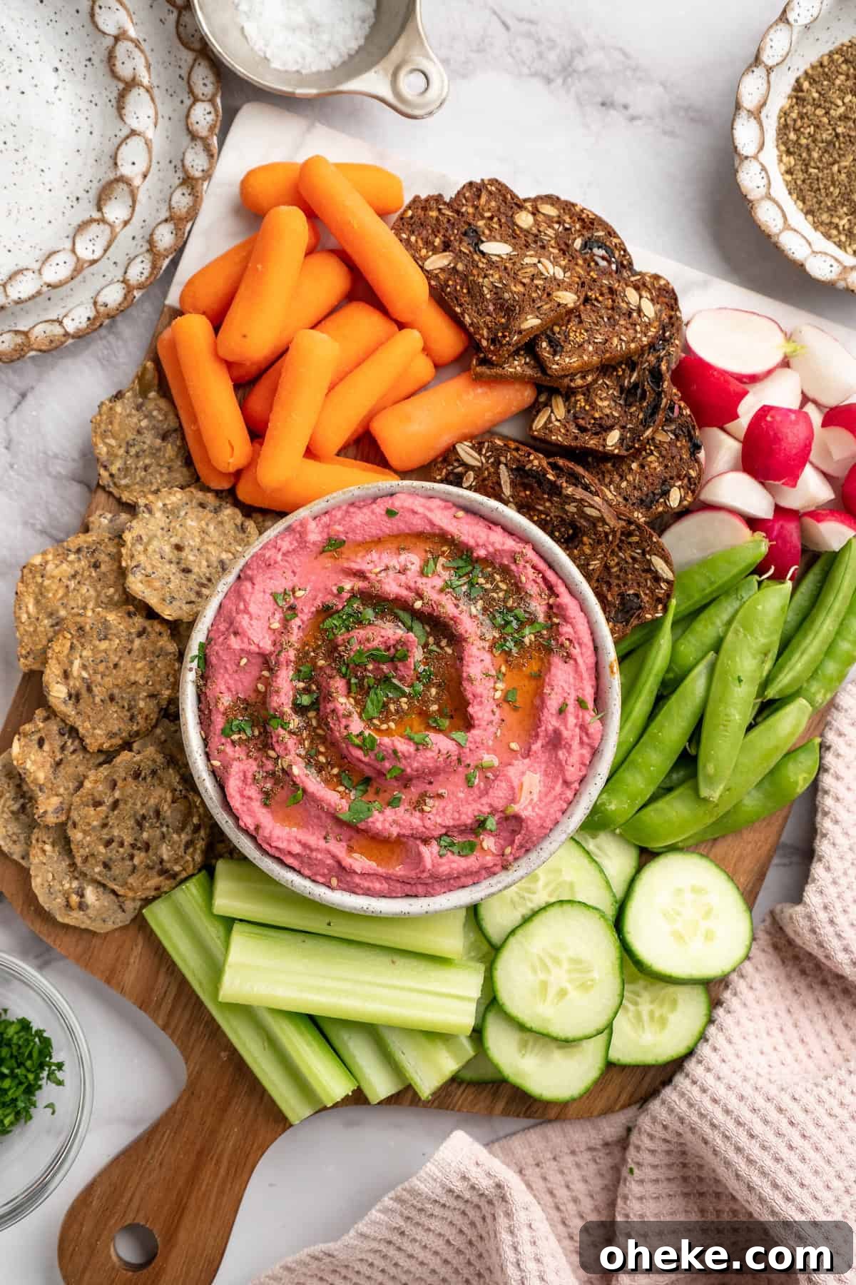 Beet hummus served with crackers and vegetables Wooden board with bowl of beet hummus, crackers, and raw vegetables