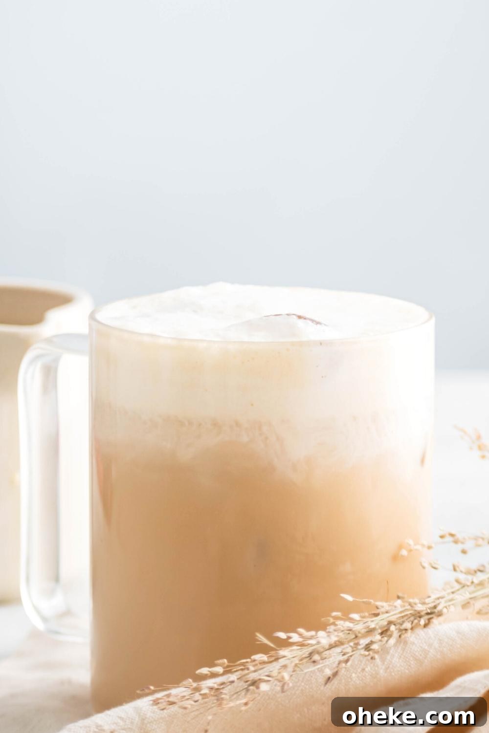 Starbucks Iced White Chocolate Mocha Copycat Recipe — How to Make at Home 8 A glass filled with an iced white chocolate mocha. In front of the bottom of it is a white tablecloth and a piece of straw.