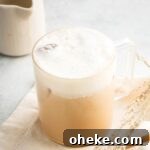 Foam on top of an iced white chocolate mocha and a glass cup that is on a white tablecloth.